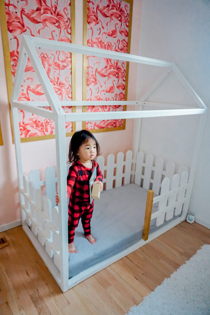 Toddler girl standing in a white Montessori style house bed