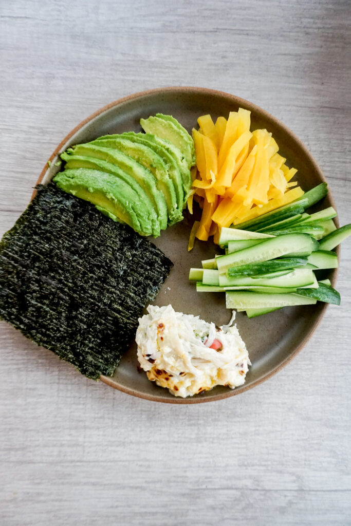 Plate of broiled sushi bake, cucumber, pickled daikon, avocado, and seaweed.