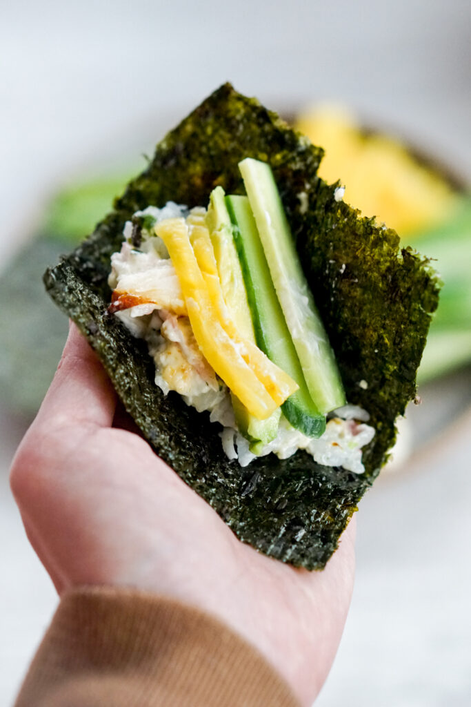 Closeup of hand holding a piece of seaweed with sushi bake and vegetables inside.