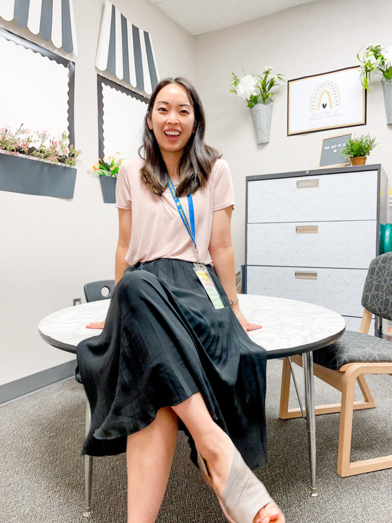 Asian woman wearing a pink Loft shirt and black Nordstrom midi skirt, sitting in a Paris themed classroom