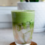 head on shot of clear glass showing iced coconut water with matcha foam layered on top