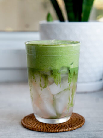 head on shot of clear glass showing iced coconut water with matcha foam layered on top